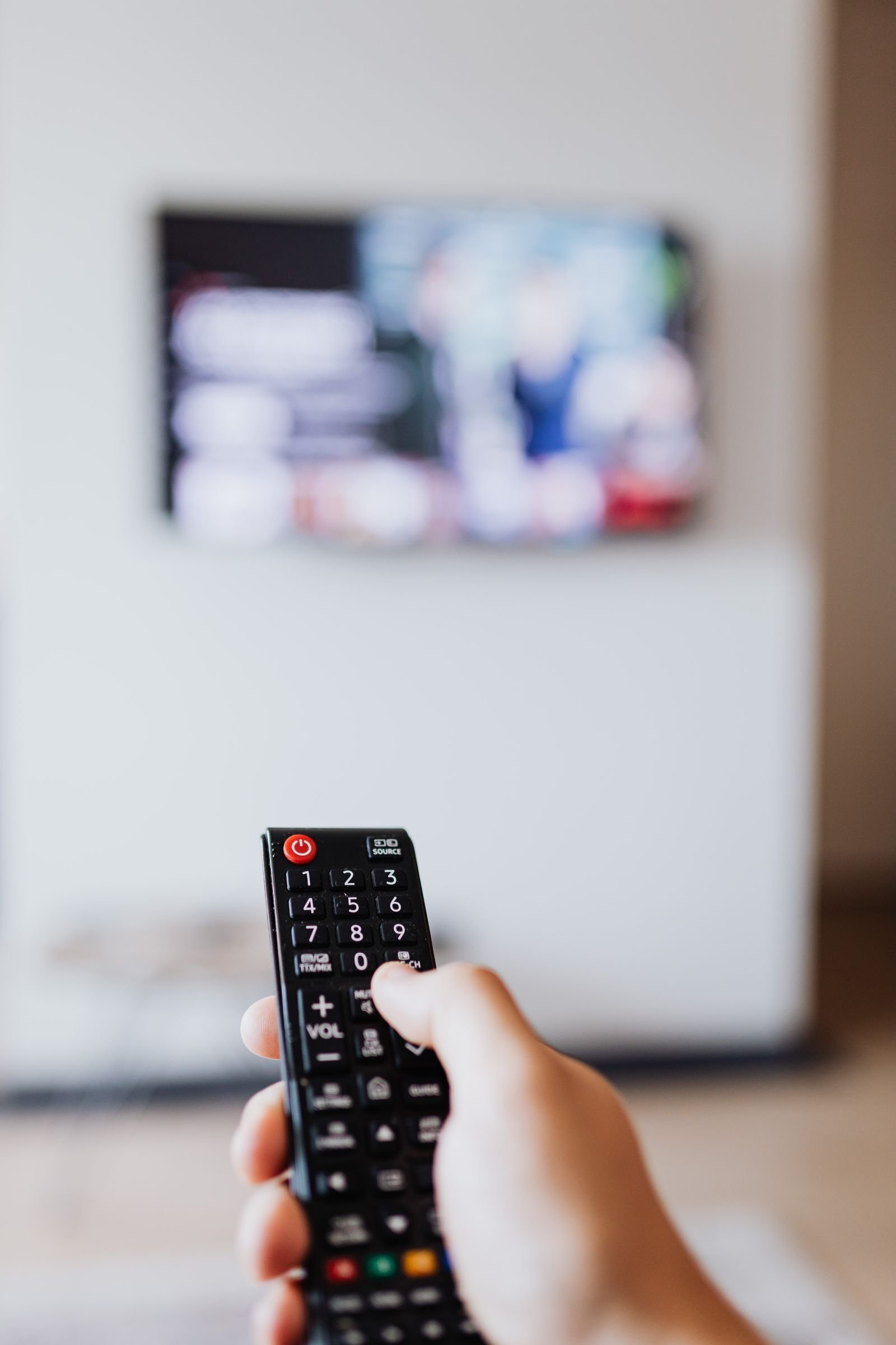Nærbilde av en hånd med fjernkontroll foran en tv, klar for viking iptv