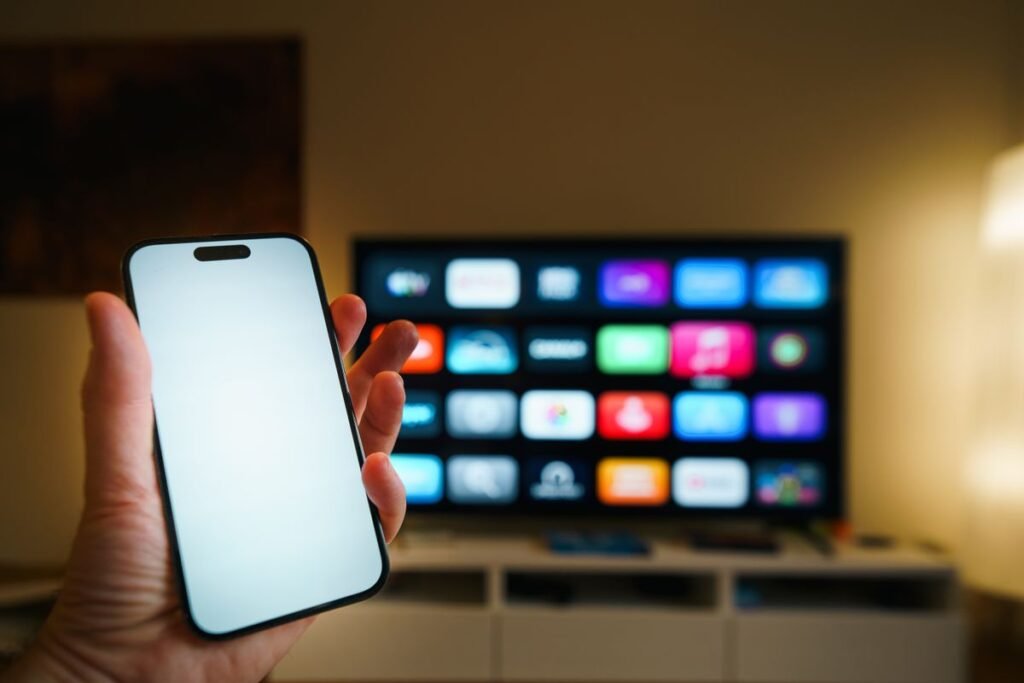 Mobil i hånden foran en smart-TV med apper, et bilde på hva iptv er i praksis